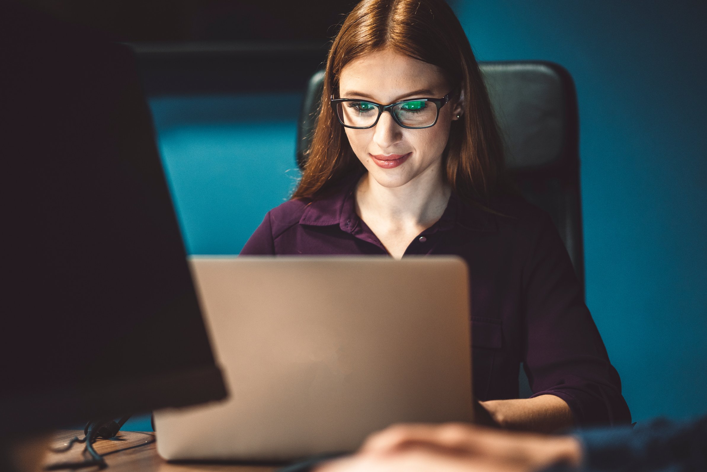 Woman tech professional with glasses looking at a laptop screen